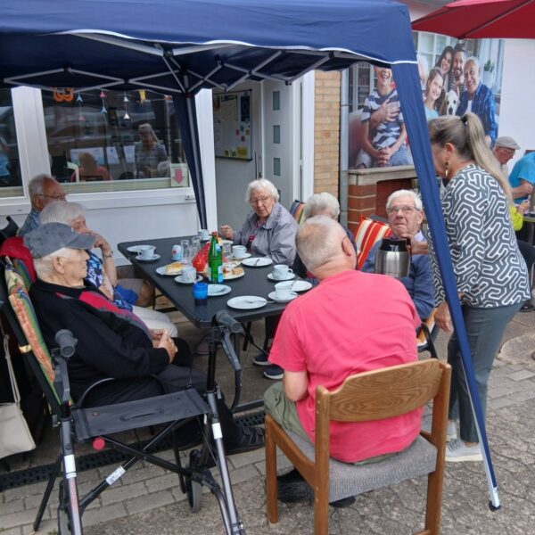 Frauen und Männer sitzen am Tisch und trinken Kaffee und essen Kuchen.