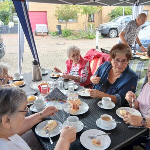 Mehrere Frauen sitzen am Tisch und trinken Kaffee und essen Kuchen. Im Hintergrund steht ein Mann.