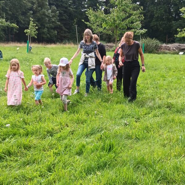 5 Kindergartenkinder und 4 Frauen laufen über eine Wiese