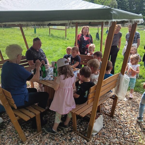 Ein paar Kindern und Erwachsene auf der Streuobstwiese an einem Pavillion bei einer Trinkpause